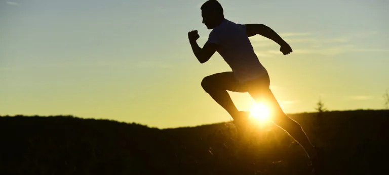 Silhouette of athlete running at sunset with backlit motion