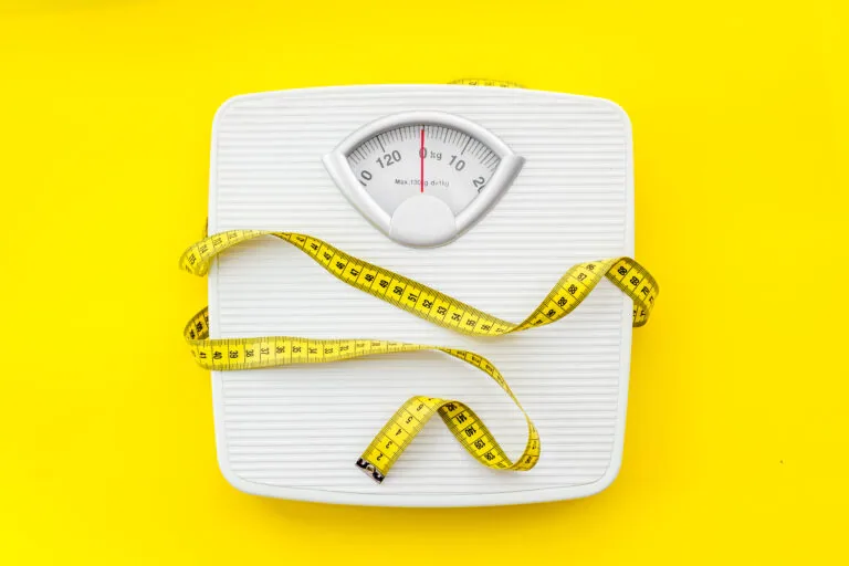 White bathroom scale with measuring tape wrapped around it on yellow background