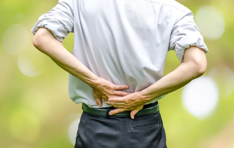 Person holding lower back with both hands, experiencing back pain or discomfort