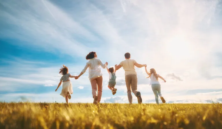 Family holding hands running together through an open field under blue sky