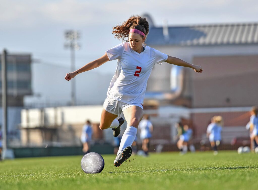 Female soccer player number 2 in white uniform kicking a ball during a match at a stadium