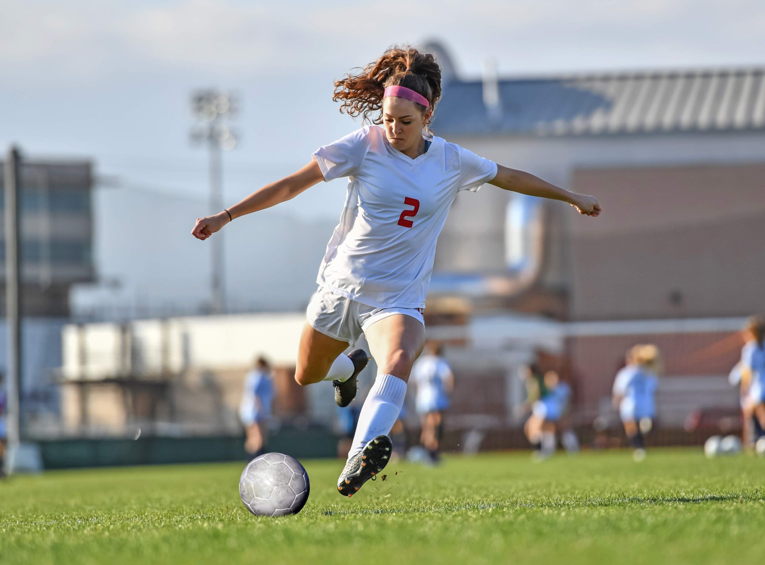 Female soccer player number 2 in white uniform kicking a ball during a match at a stadium