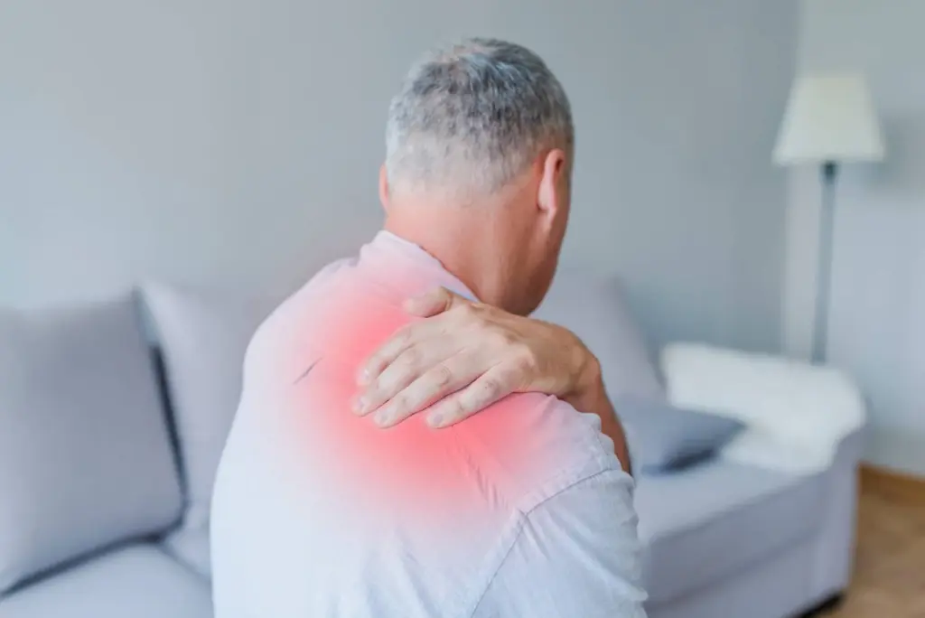 A man on his sofa holding a sore shoulder, the painful spot glowing red