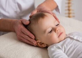 Adult hands gently cradling a sleeping infant's head during a medical examination or treatment