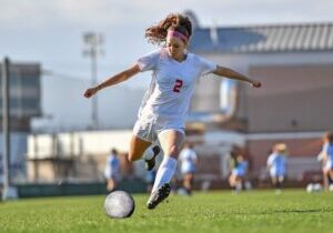 Female soccer player number 2 in white uniform kicking a ball during a match at a stadium